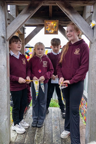 4 students standing under a wooden hut outside